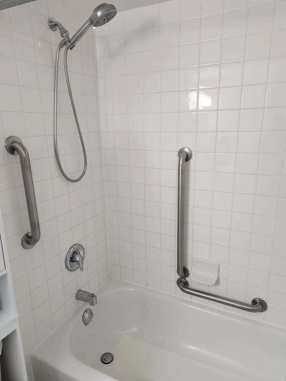 A Westlake install: white-tiled tub and shower fitted with two stainless grab bars and a slide-bar handheld shower head