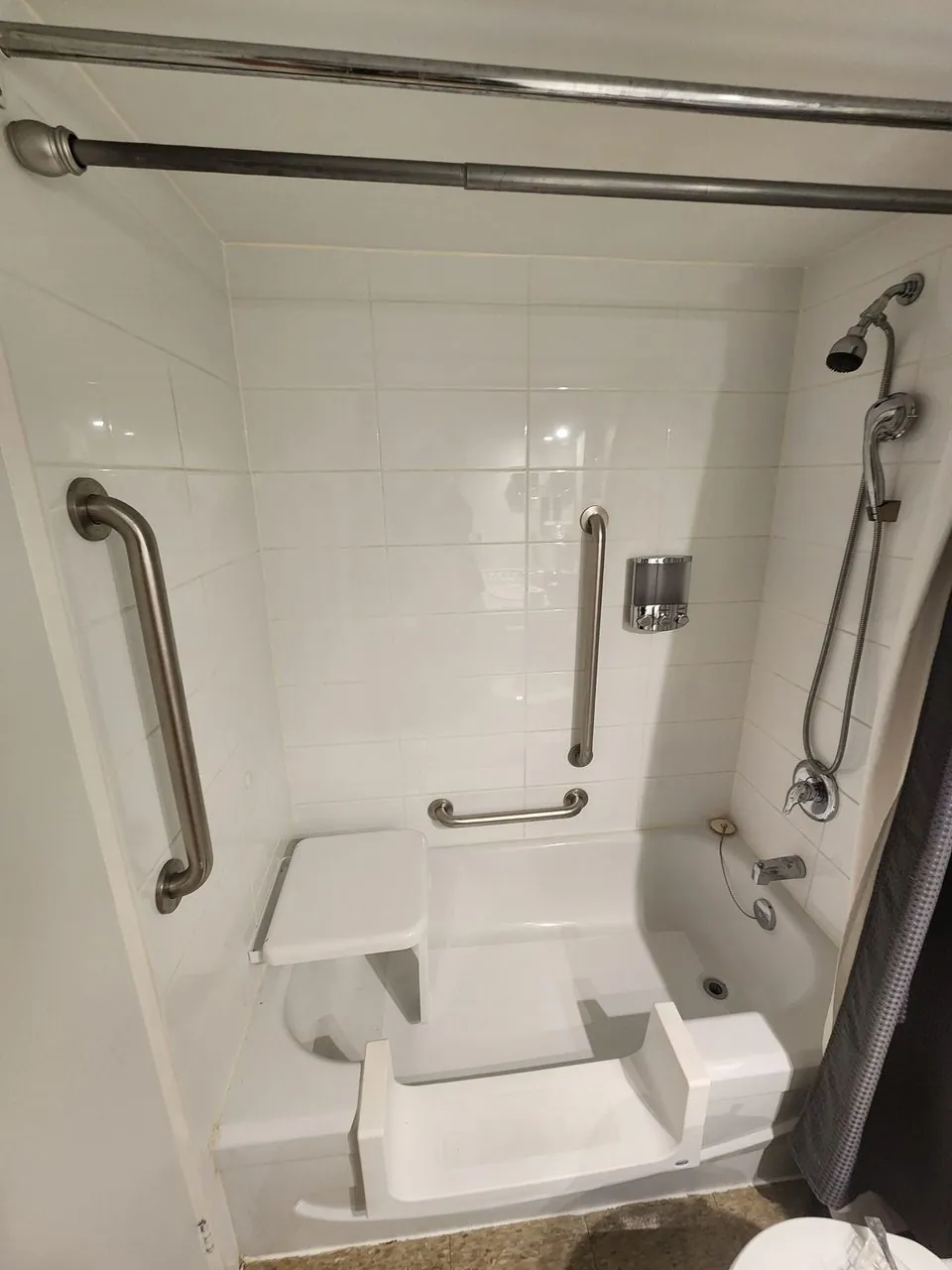 A converted tub-to-shower with a low step-through entry, grab bars and a handheld shower head